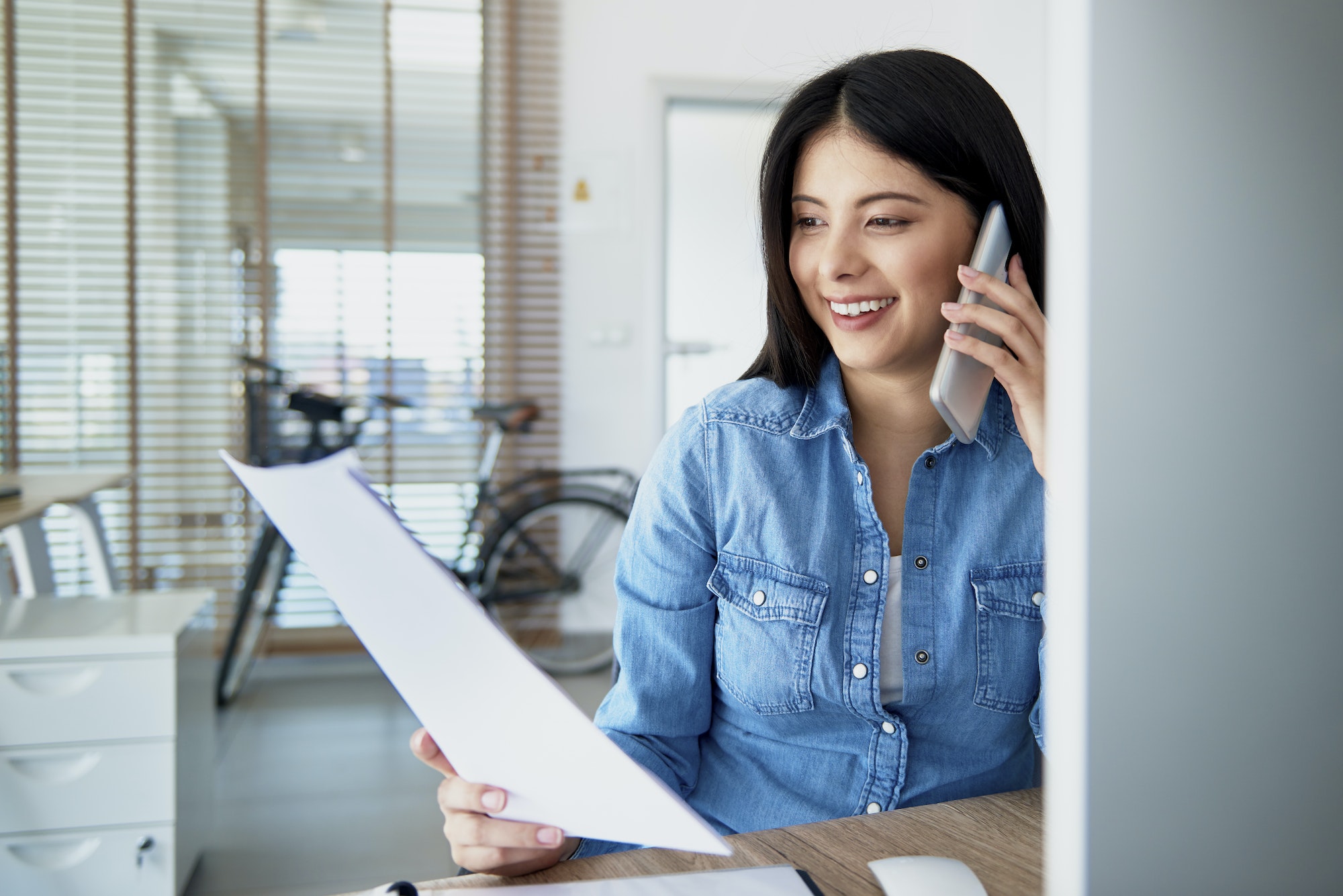 Cheerful Asian woman in the office talking on the phone